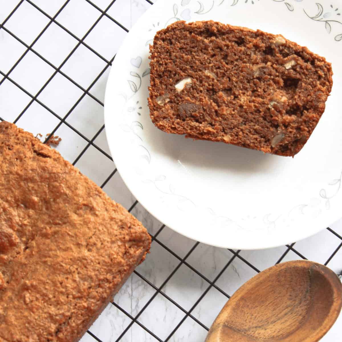 overhead image of a loaf of cinnamon pecan banana bread on wire cooling rack with sliced piece to the side and wooden spoon peeking in from the bottom