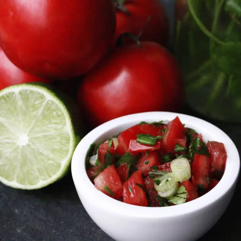 pico de gallo in small white bowl and tomatoes and sliced lime in background