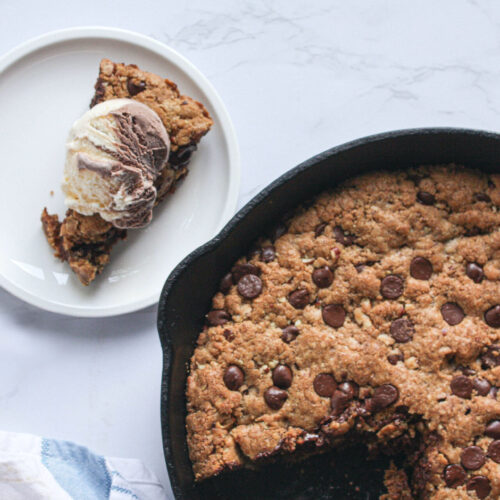 cookie in a large cast iron skillet with a slice removed and topped with ice cream | hearth health happiness