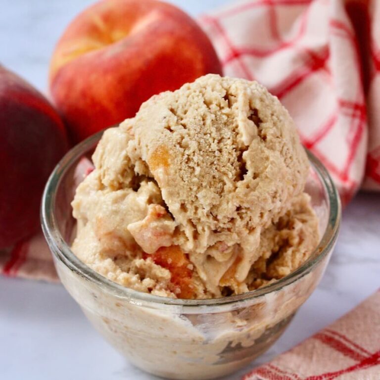 Scoop of coconut peach ice cream in glass bowl on counter with peaches