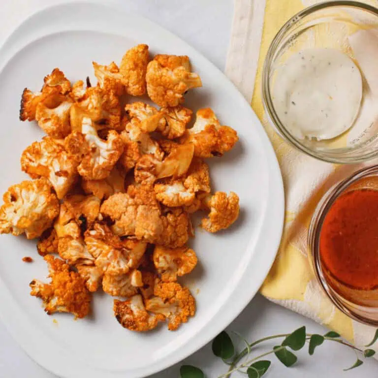 overhead image of buffalo cauliflower bites on platter with dipping sauces to the side