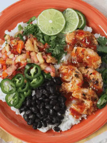 overhead image of plant-based fiesta coconut shrimp on plate with pineapple salsa, rice, black beans, and lime slices