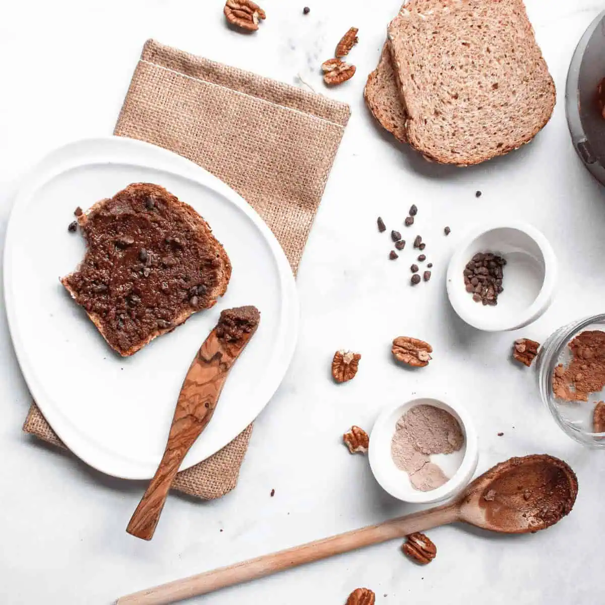 overhead image of triple chocolate pecan spread on toast with ingredients scattered on counter