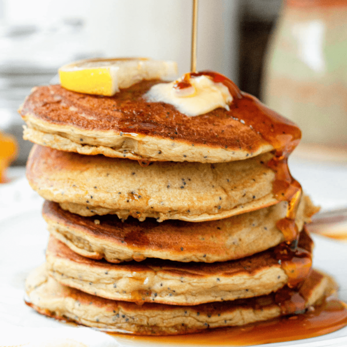 Stack of vegan lemon poppy seed pancakes on counter with syrup drizzle