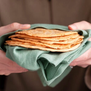 holding a stack of red lentil tortillas in green tea towel