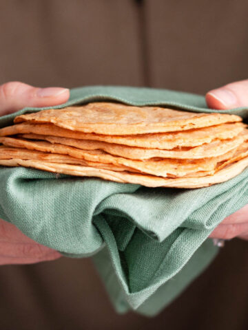 holding a stack of red lentil tortillas in green tea towel