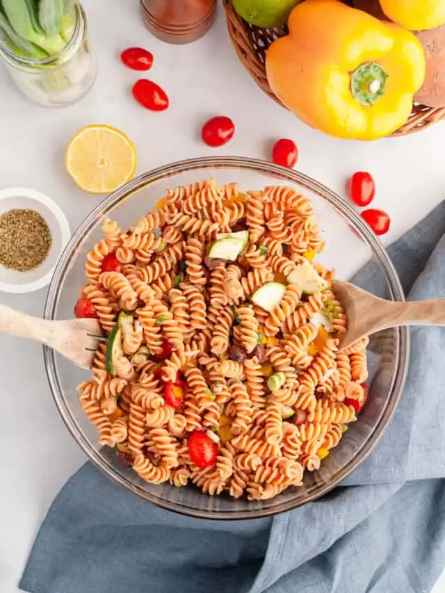 vertical image of red lentil pasta salad in bowl with wooden utensils to toss