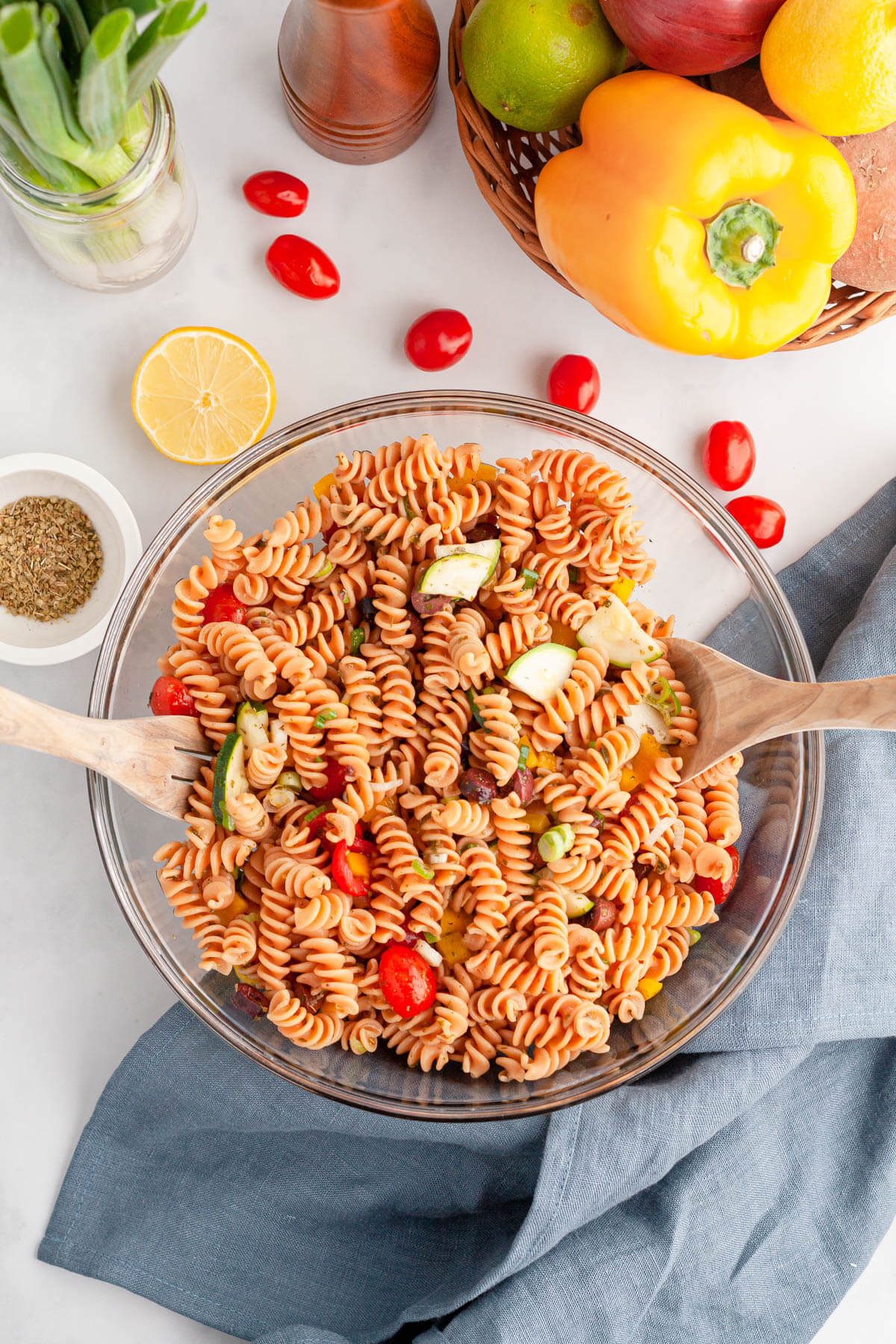 vertical image of red lentil pasta salad in bowl with wooden utensils to toss