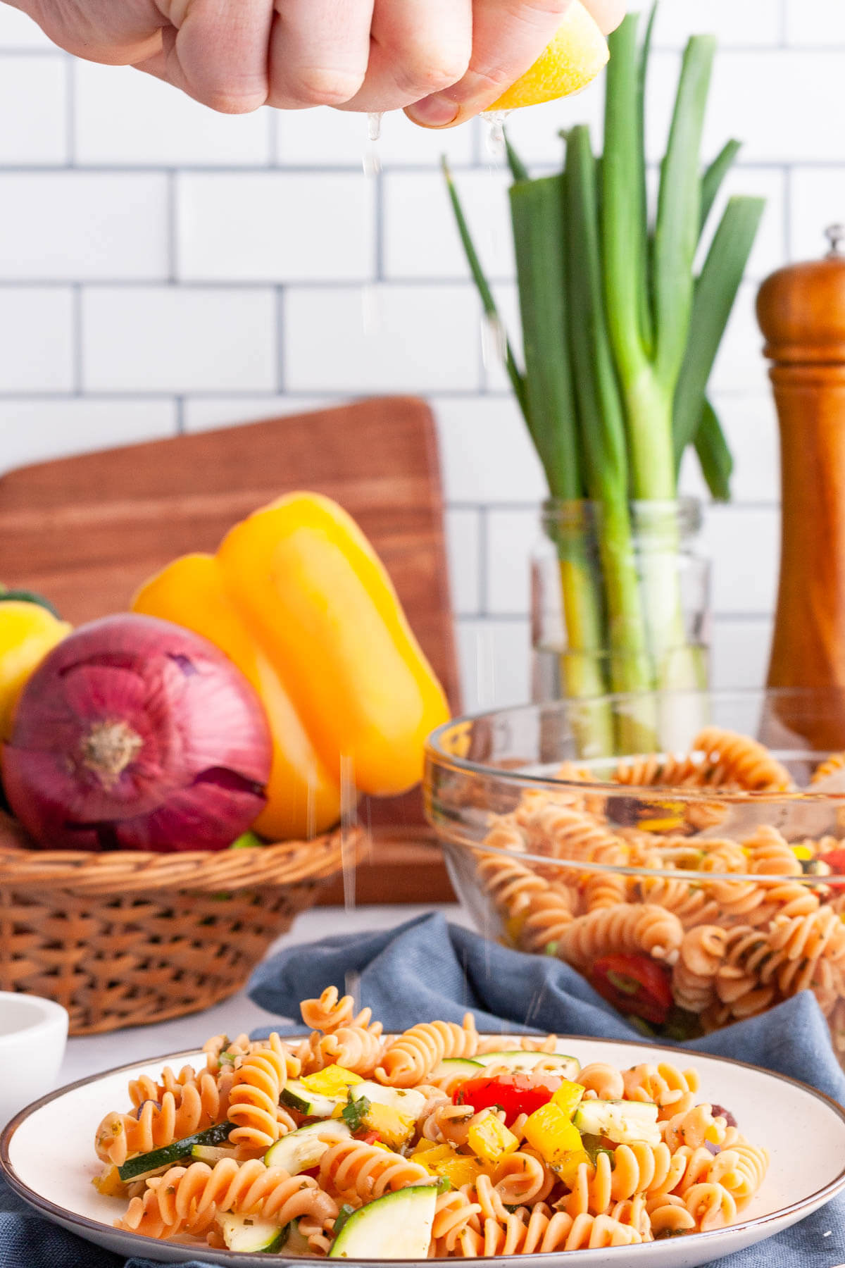 hand squeezing lemon over red lentil pasta salad on plate