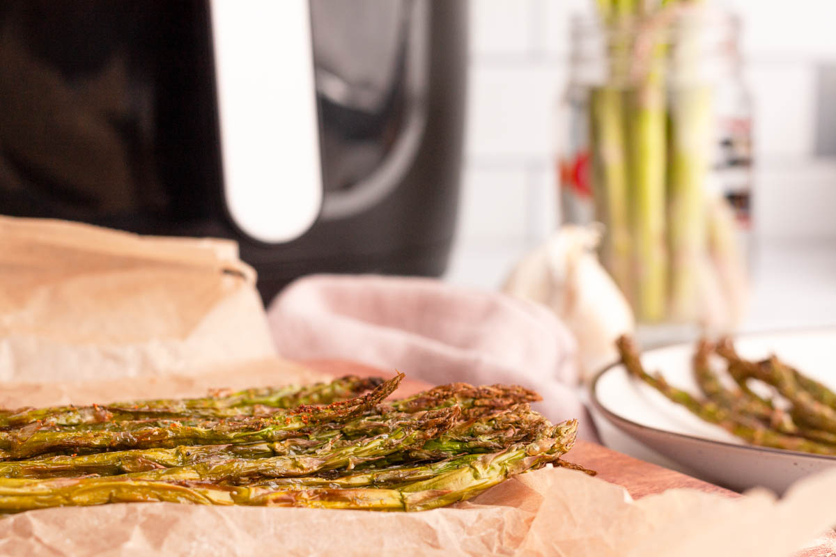 air fryer asparagus stalks on plate with air fryer in the background