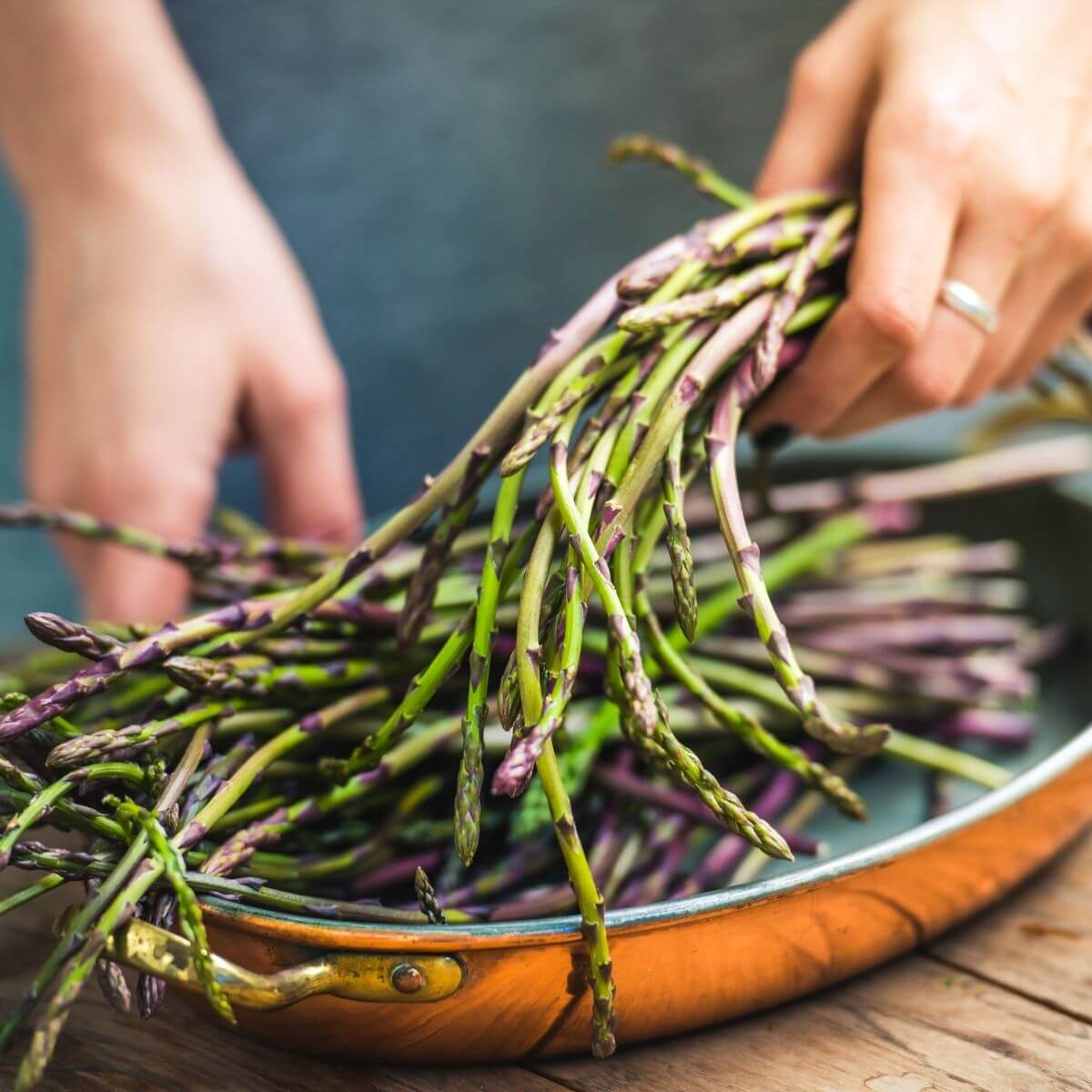 asparagus in copper skillet being grasped by 2 hands