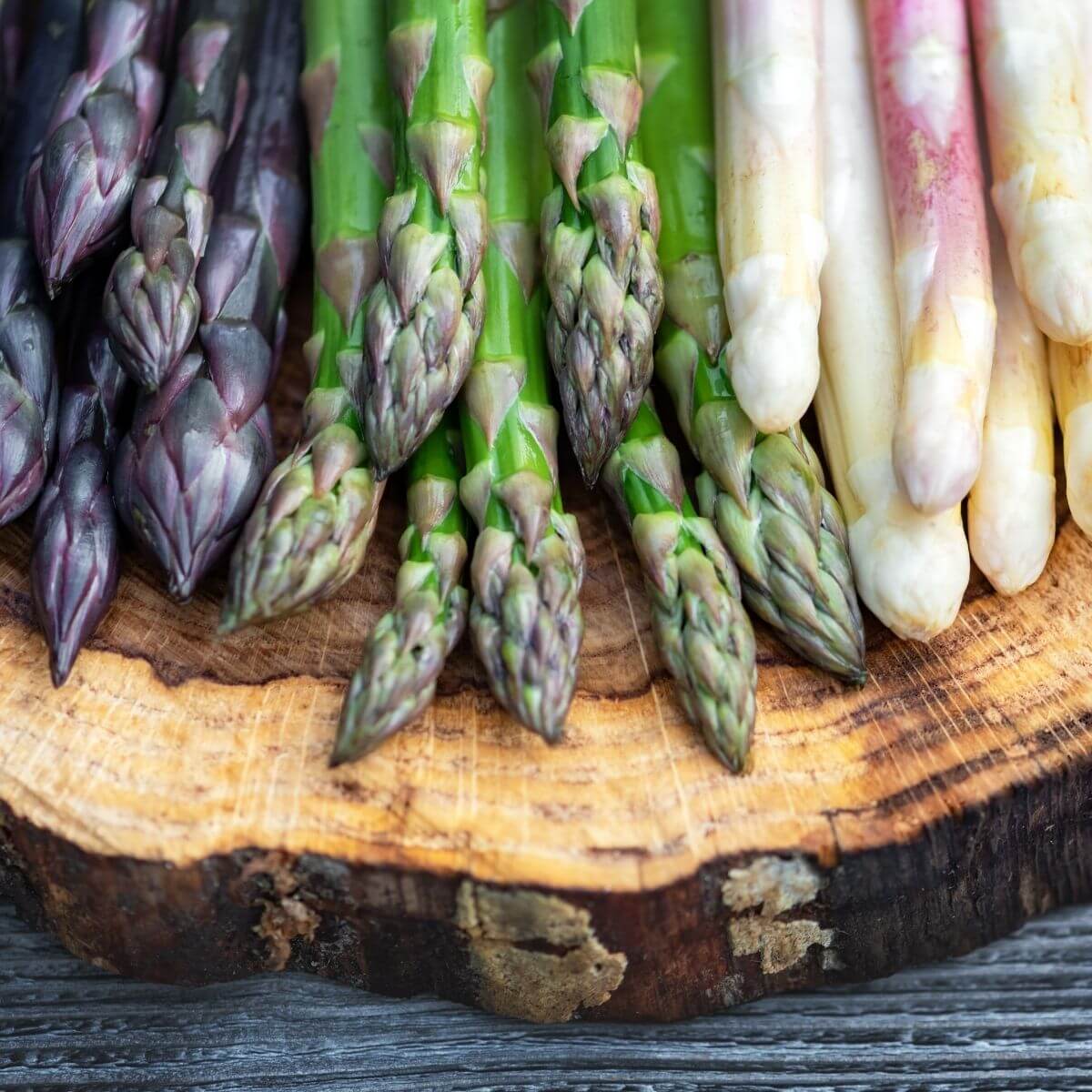 purple green and white asparagus on wooden platter