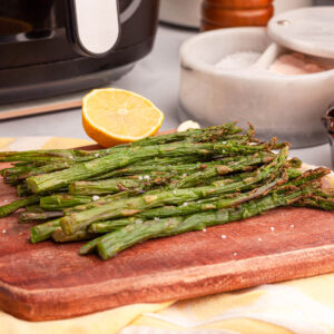 side image of air fried asparagus on serving dish with air fryer in the background