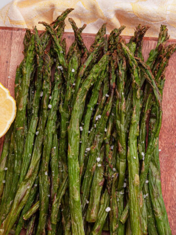 overhead image of air fryer frozen asparagus after cooking on wood board with lemon wedge
