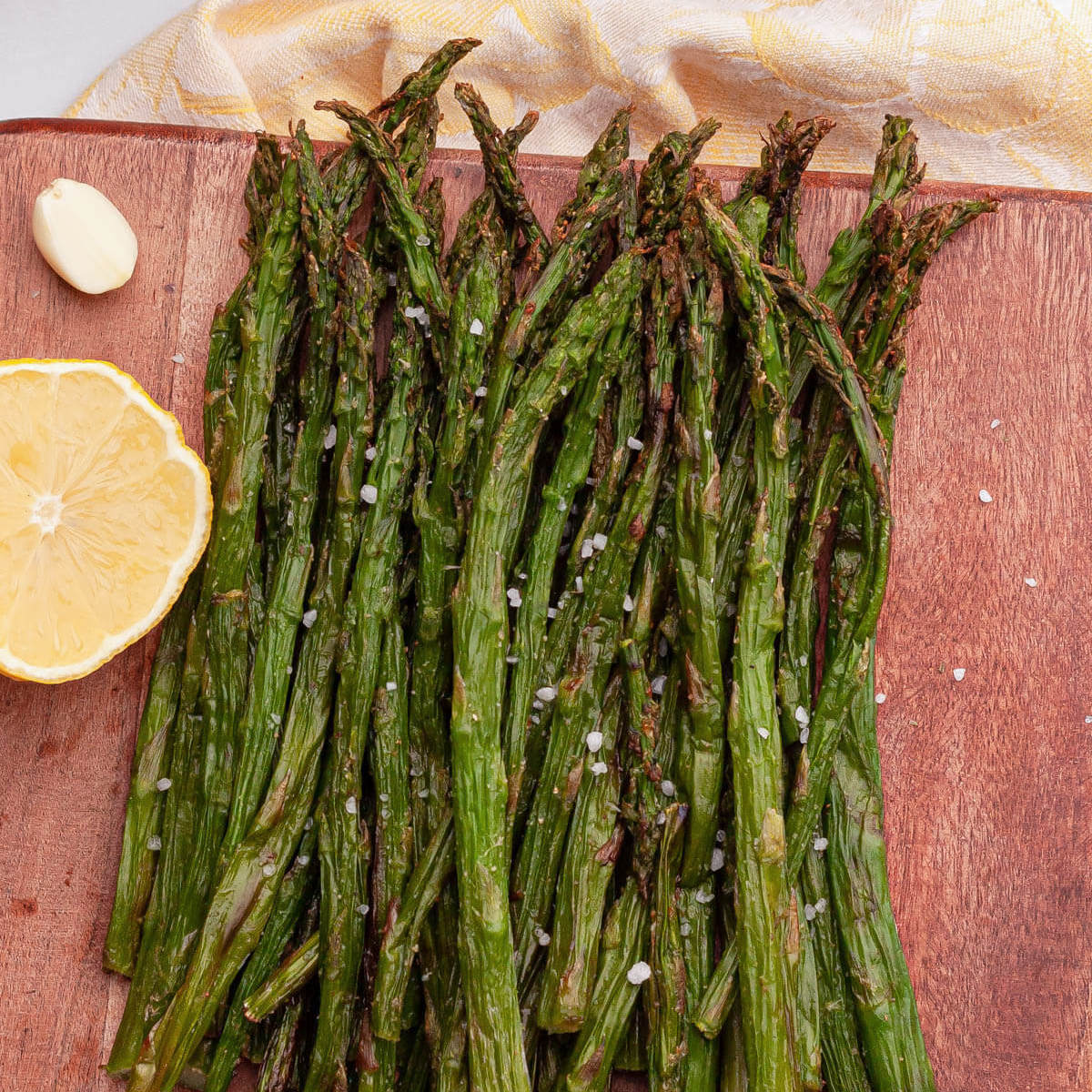 overhead image of air fryer frozen asparagus after cooking on wood board with lemon wedge