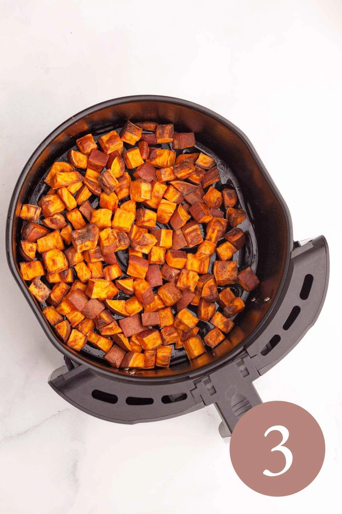overhead image of fried sweet potato cubes in air fryer basket
