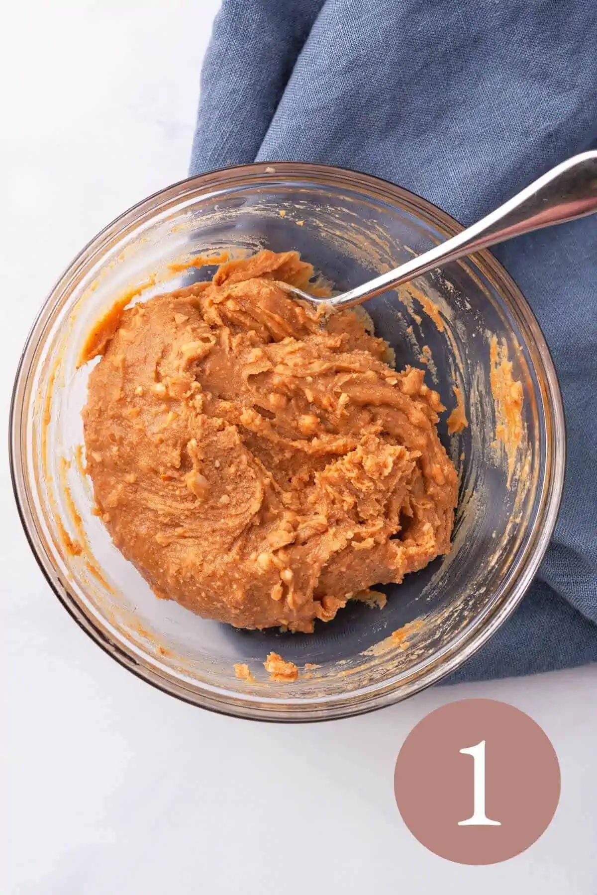 Overhead image of peanut butter and maple syrup mixed in a bowl with spoon. 