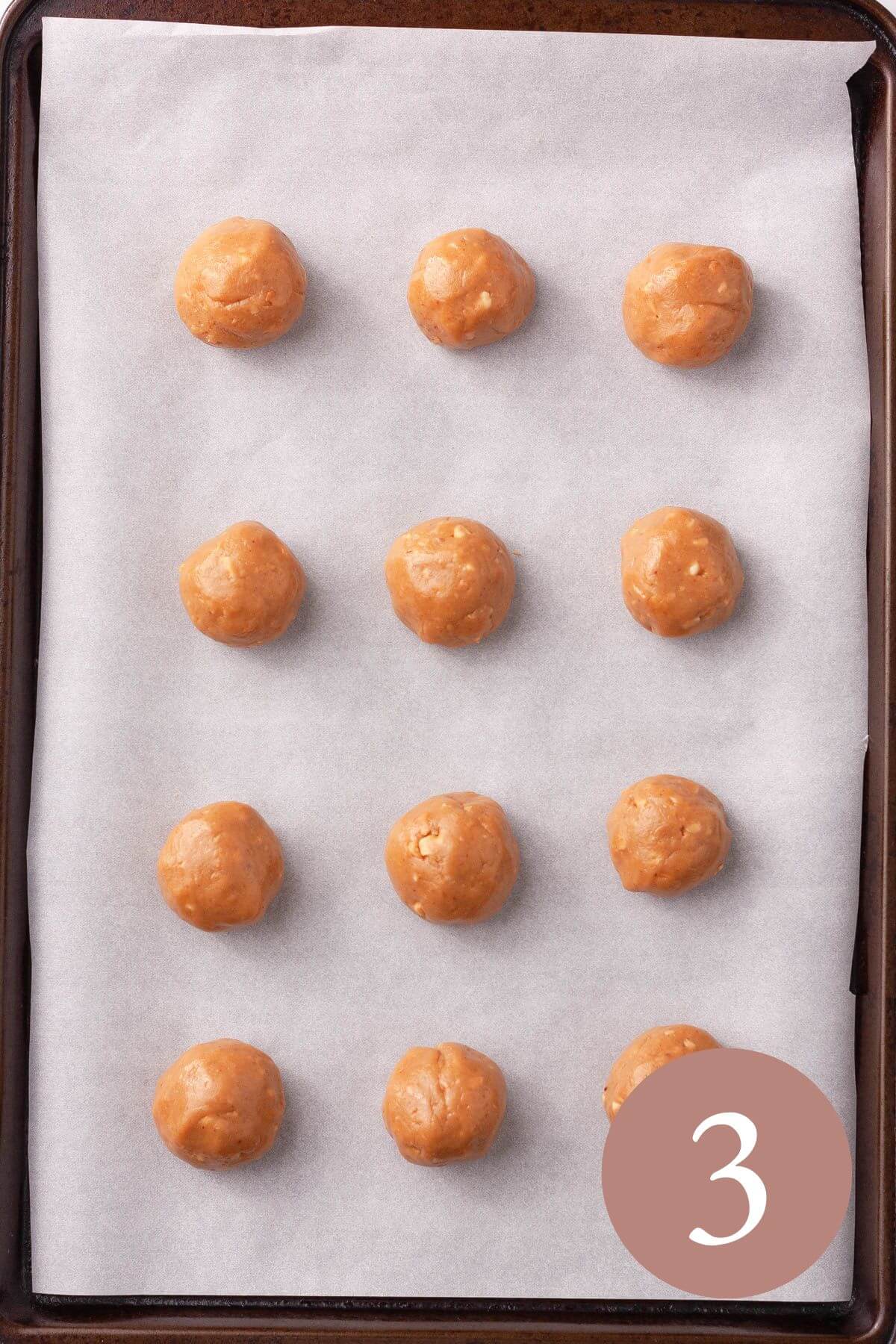 Overhead image of 12 peanut butter cookie dough balls on cookie sheet lined with parchment paper.