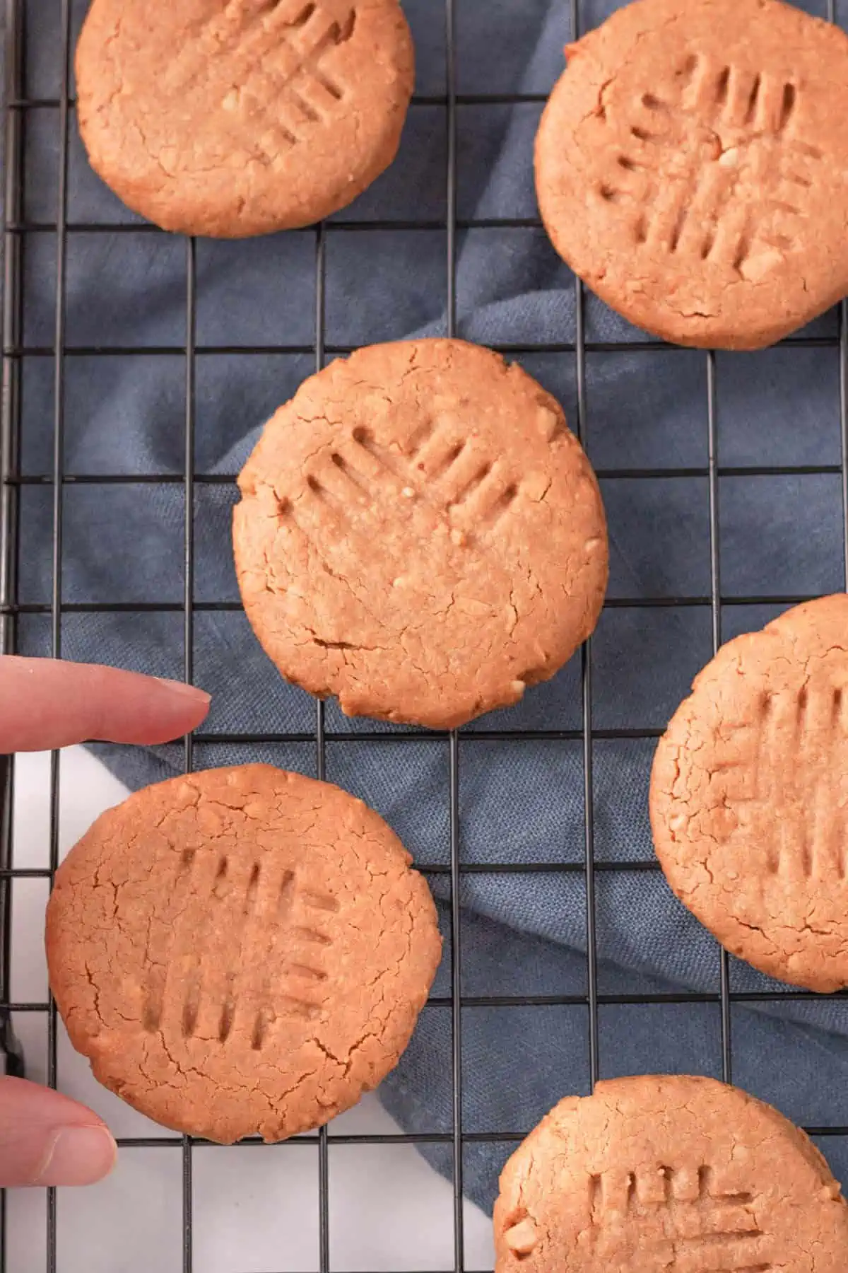 overhead image of hand reaching for peanut butter cookie on wire cooling rack