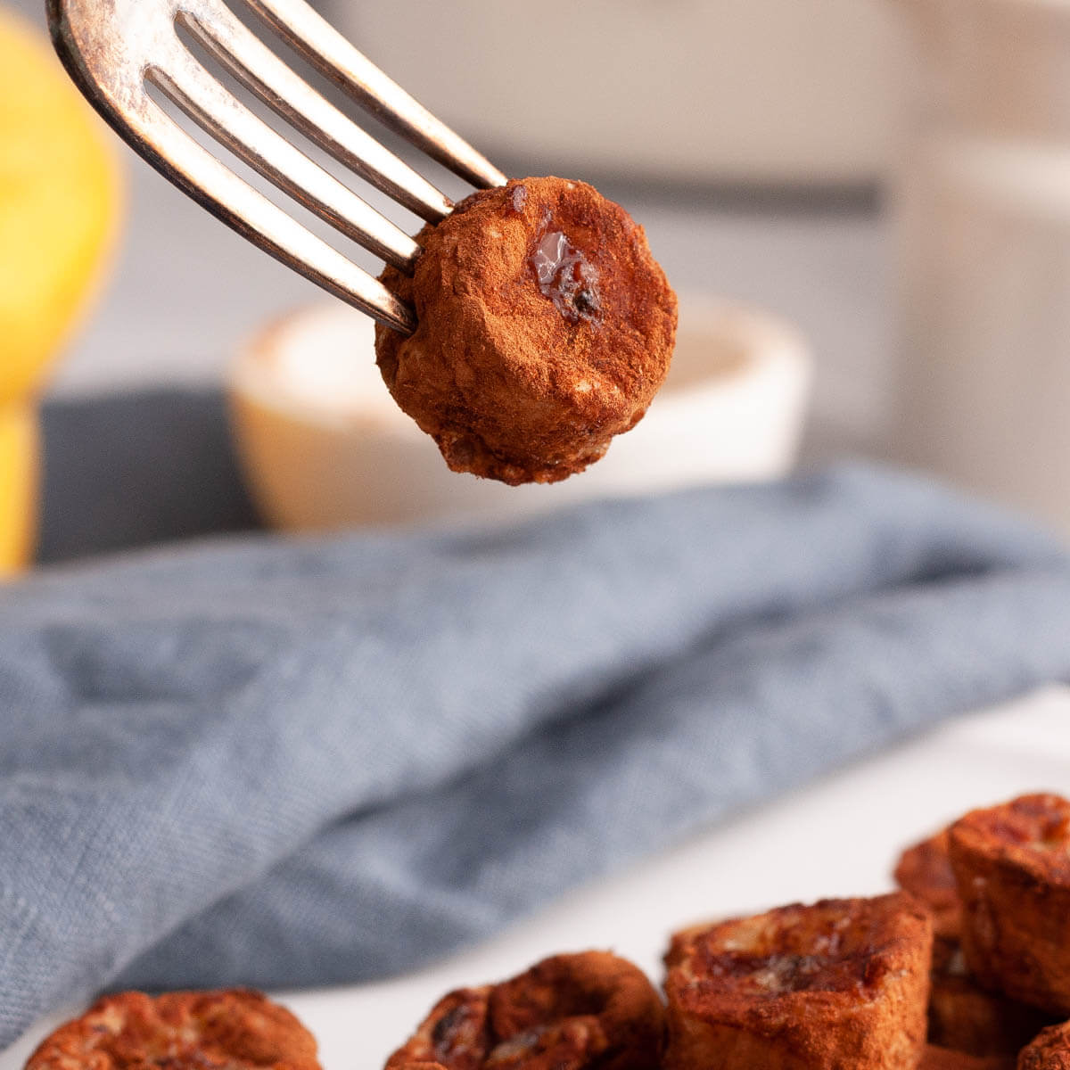 side image of air fried banana piece on fork dangling above plate