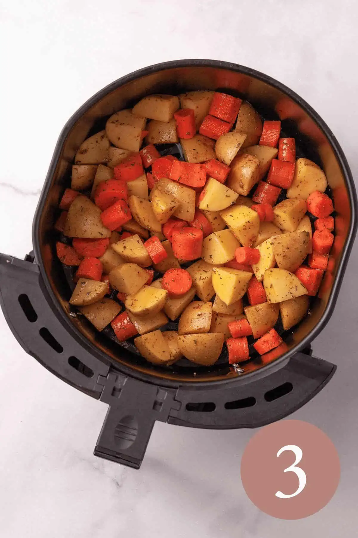 Overhead image of chopped potatoes and carrots in basket of air fryer before frying