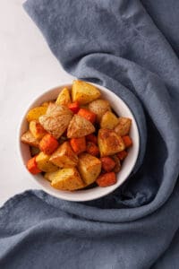 overhead image of air fried potatoes and carrots in white serving bowl near blue tea towel