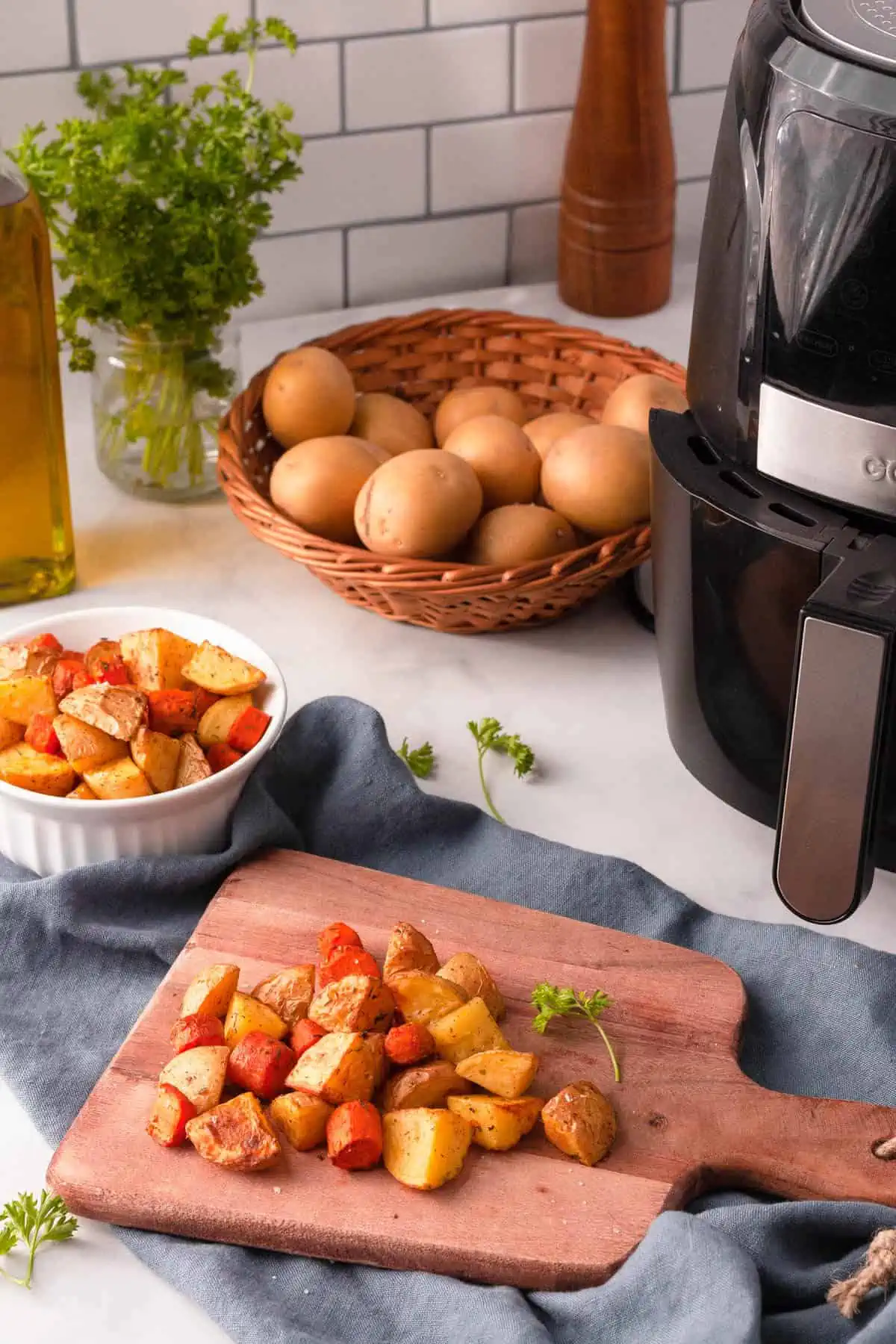 Air fried potatoes and carrots on cutting board next to air fryer and basket of potatoes