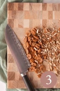 Overhead image of pecans partially chopped on cutting board with knife set aside