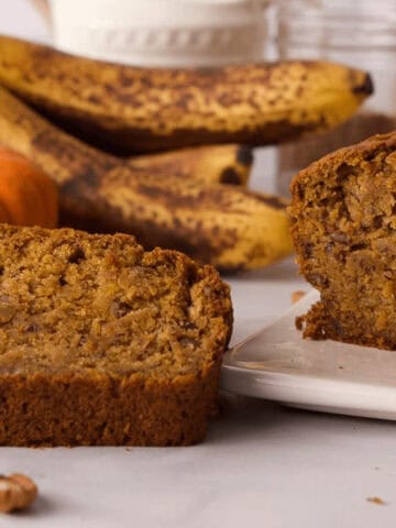 pumpkin banana bread loaf and slice propped next to it with ingredients in the background on counter