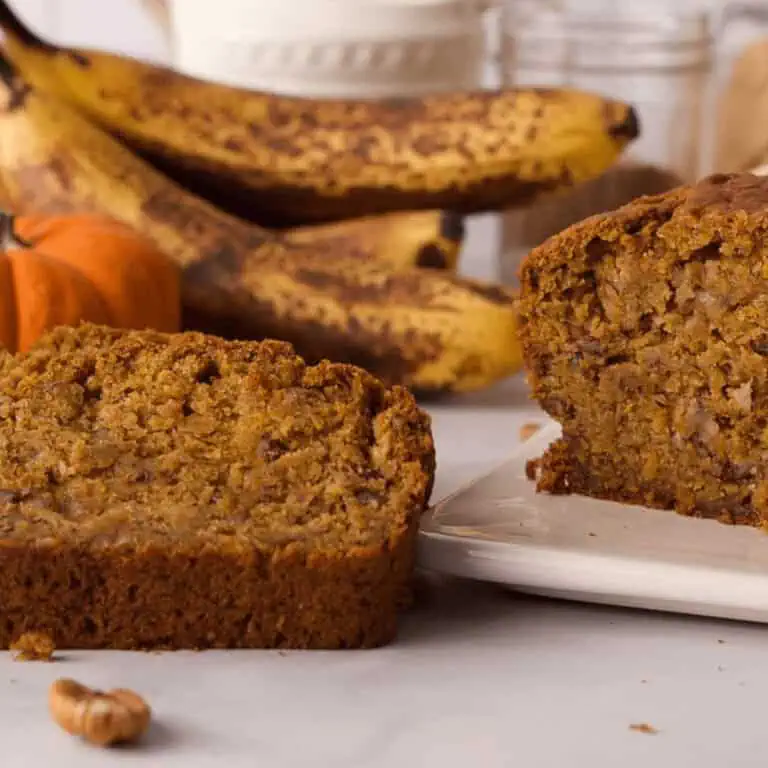 pumpkin banana bread loaf and slice propped next to it with ingredients in the background on counter