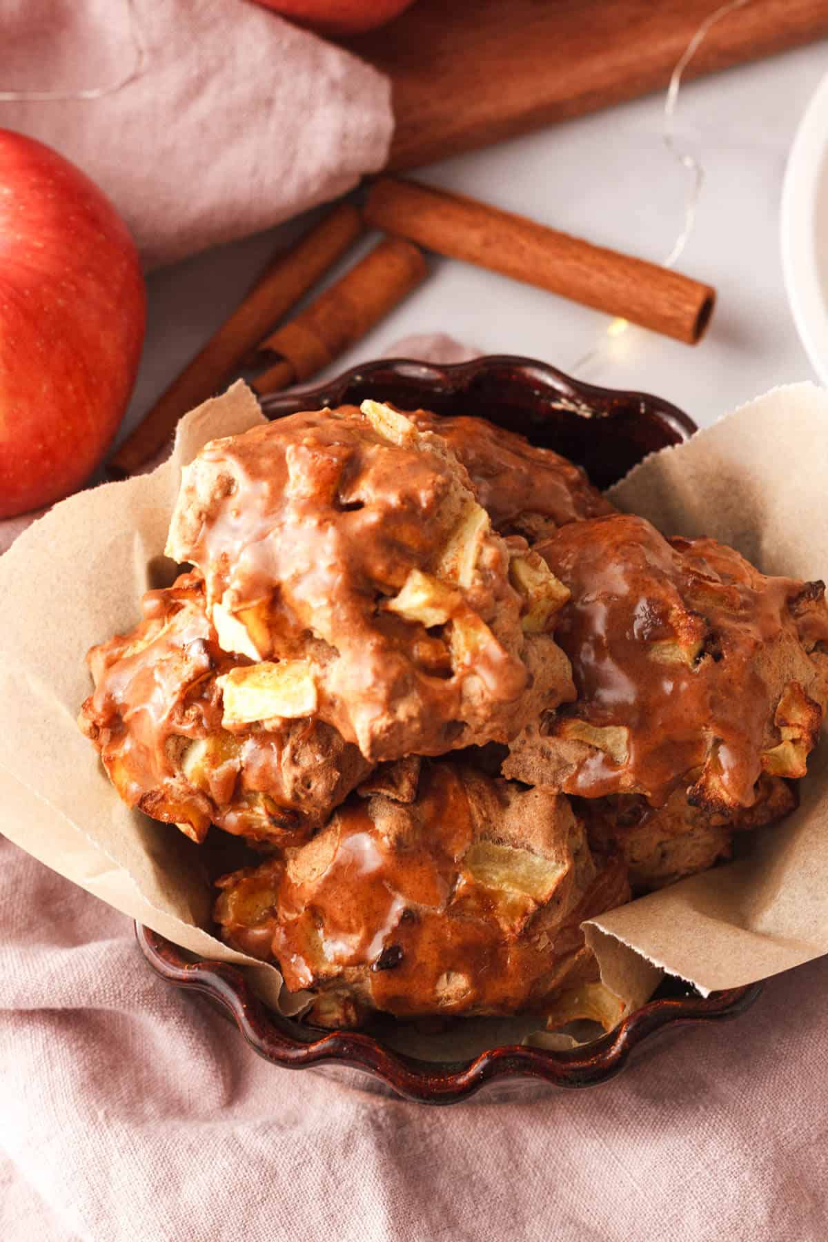 angled overhead image of applesauce fritters with glaze stacked in a baking dish lined with parchment paper