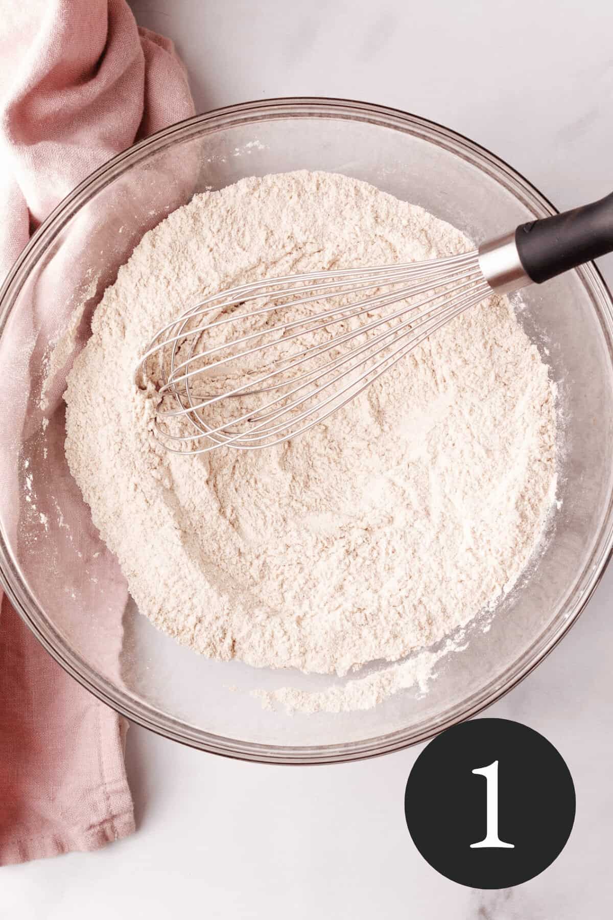 overhead image of dry ingredients in large glass bowl with whisk resting along the edge