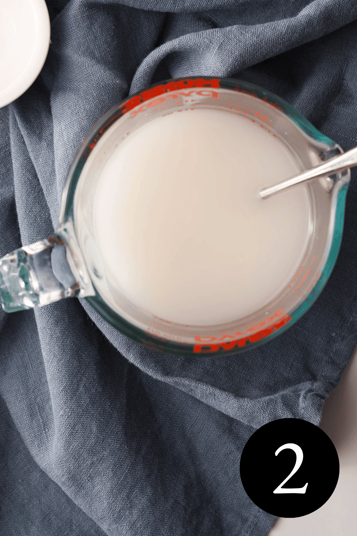 overhead image of spoon resting in liquid measuring cup holding plant-based milk and lemon juice