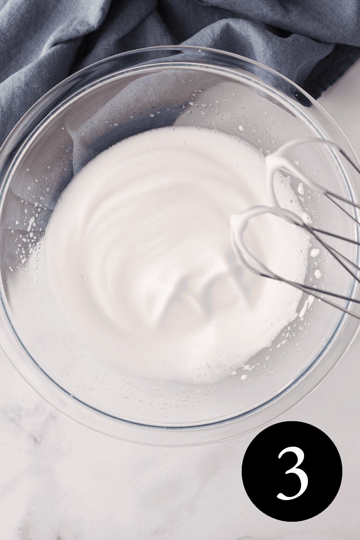 overhead image of whipped aquafaba in bowl with hand mixer beaters propped on edge of bowl