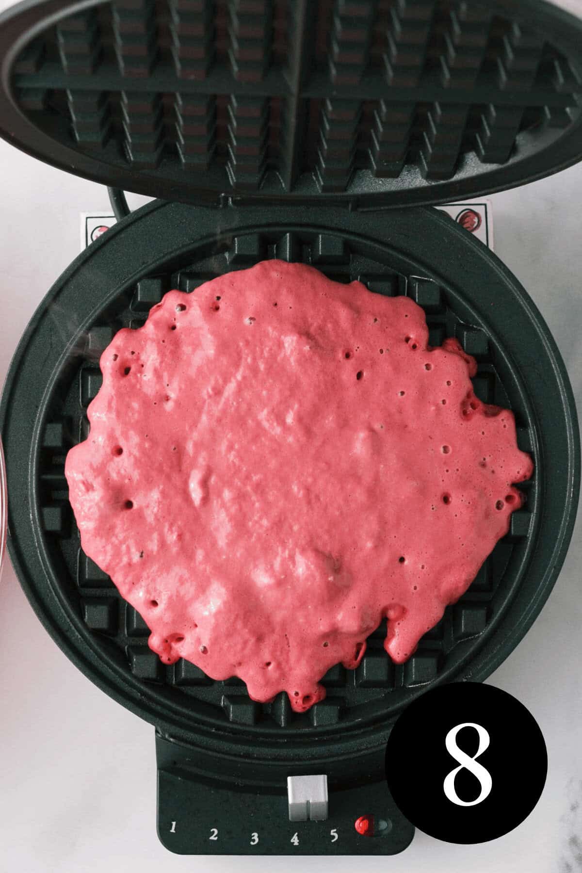 overhead image of waffle batter baking in waffle iron 