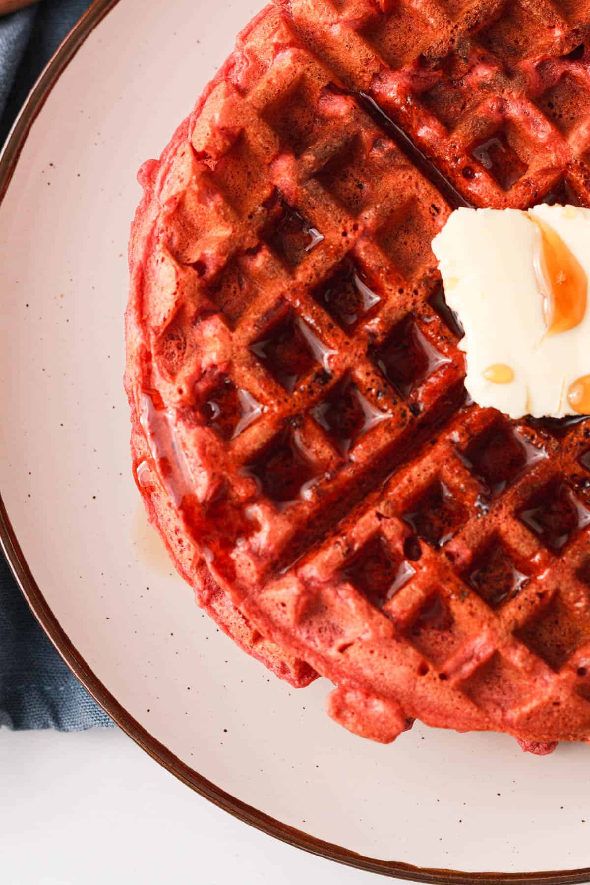 overhead closeup image of beetroot waffle with butter and syrup poured over the top
