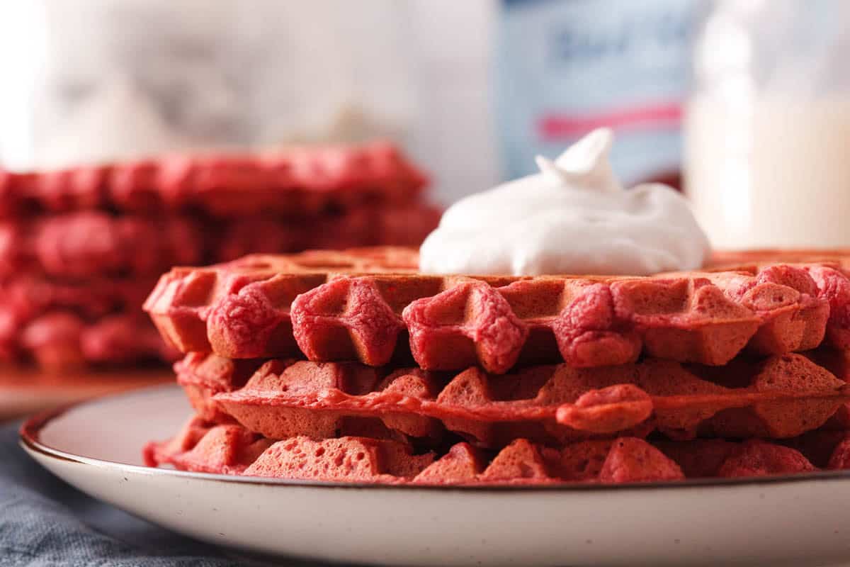 side image of stacked beetroot waffles on plate with coconut whipped topping