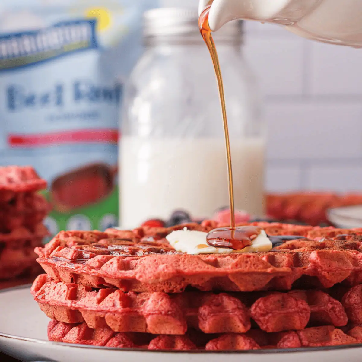 side image of stacked beetroot waffles with syrup pouring over the top