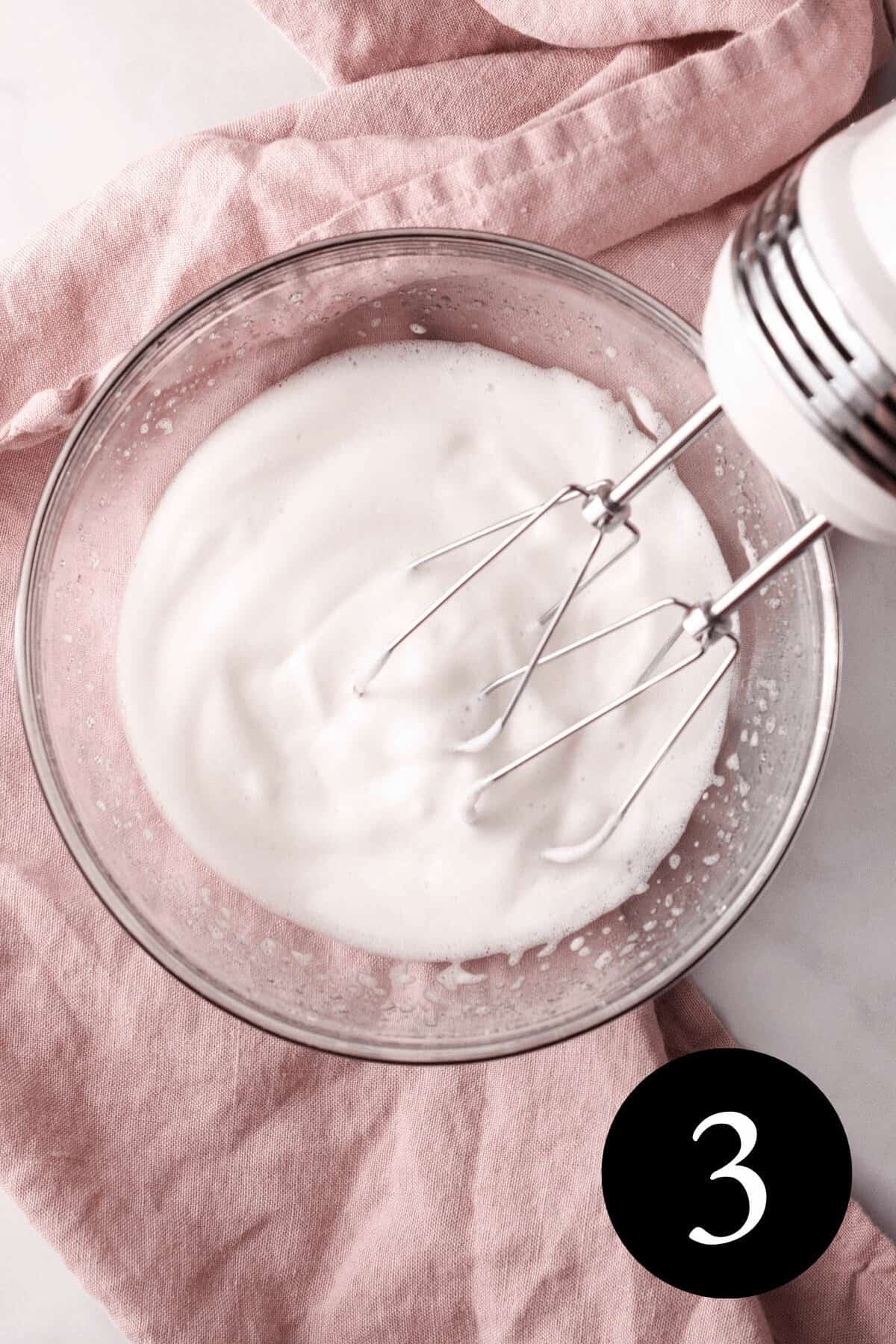 overhead image of whipped aquafaba in small bowl with hand mixer propped on the edge