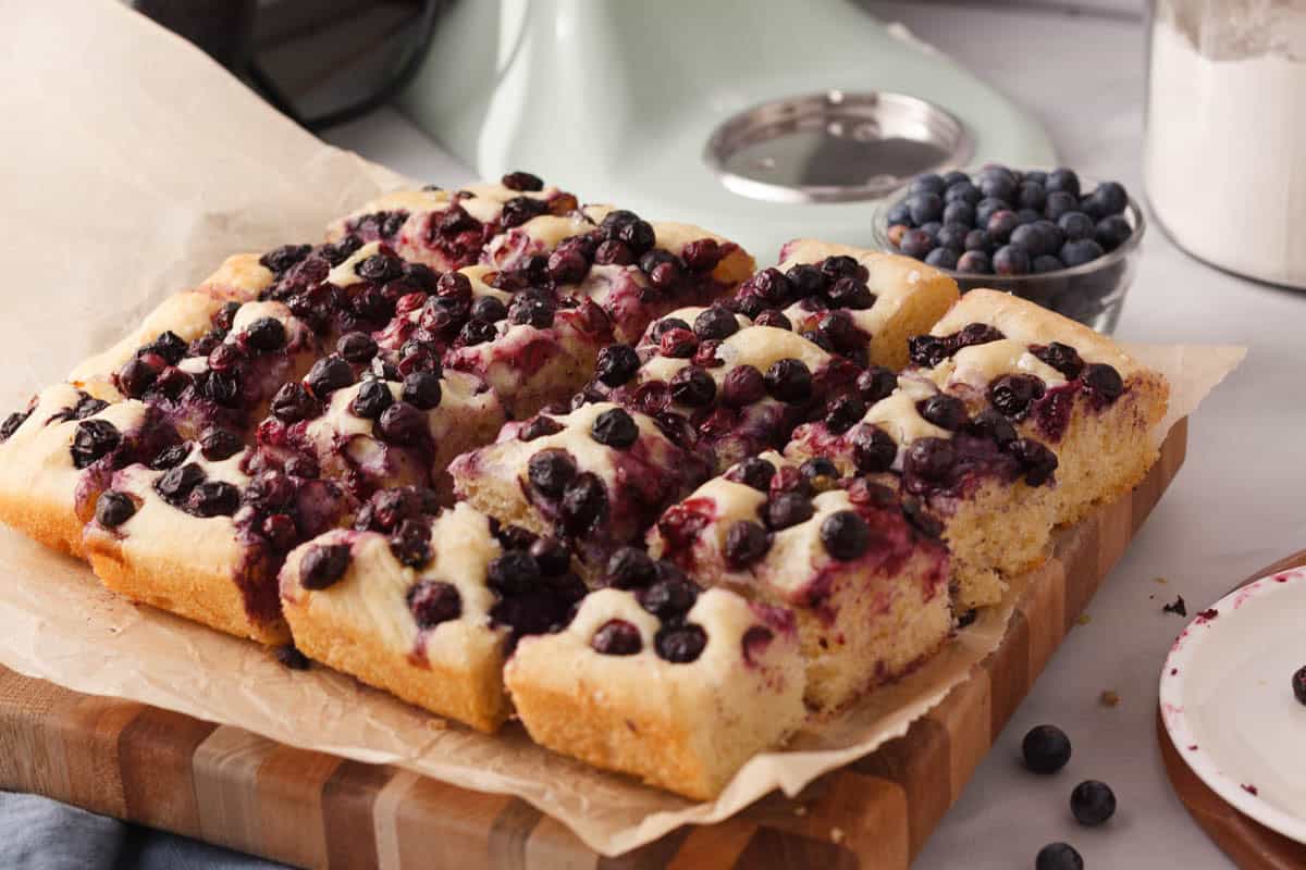 angled image of blueberry focaccia sliced into individual squares and sitting on a parchment-lined cutting board