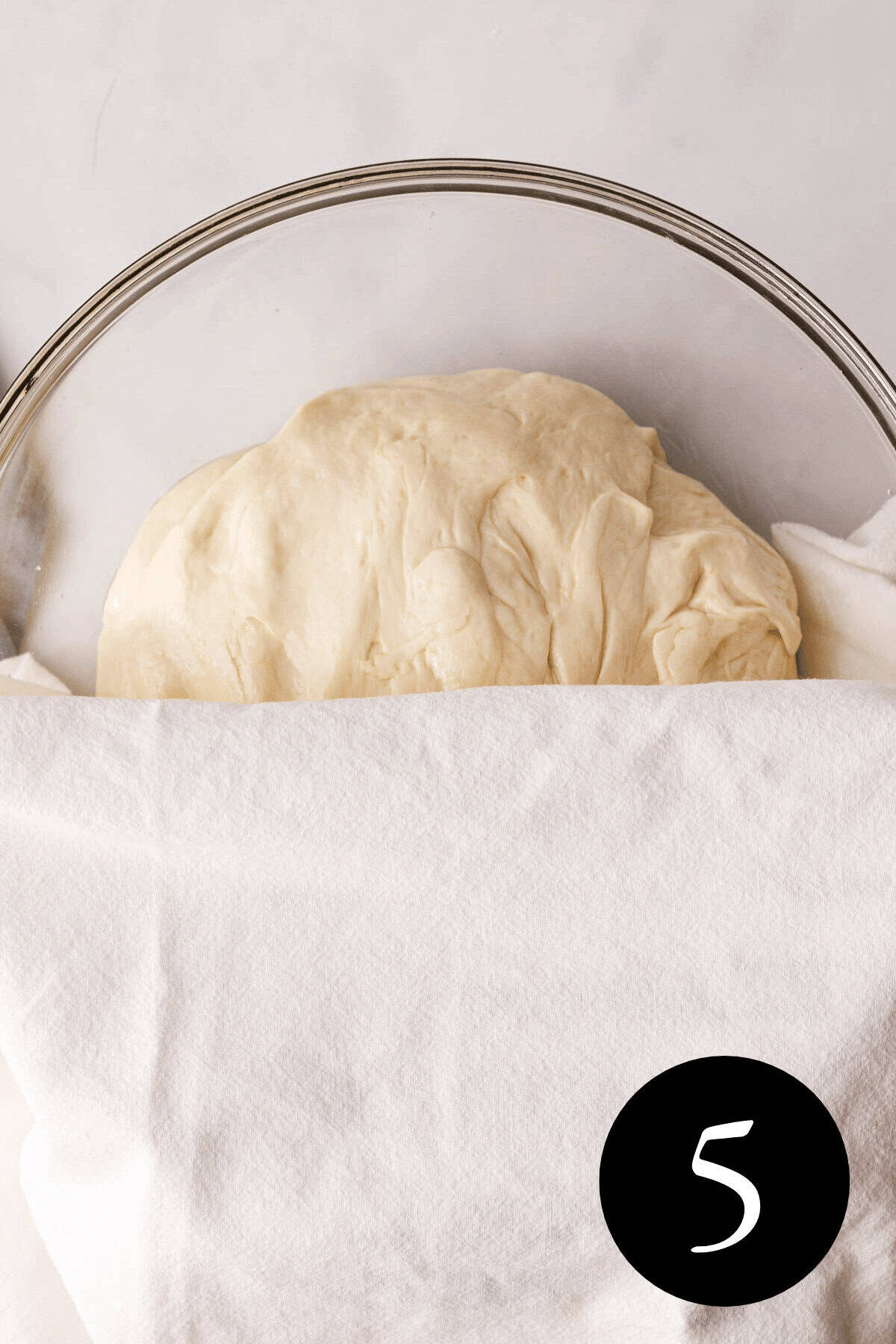 overhead image of focaccia dough in bowl with towel covering the bottom half
