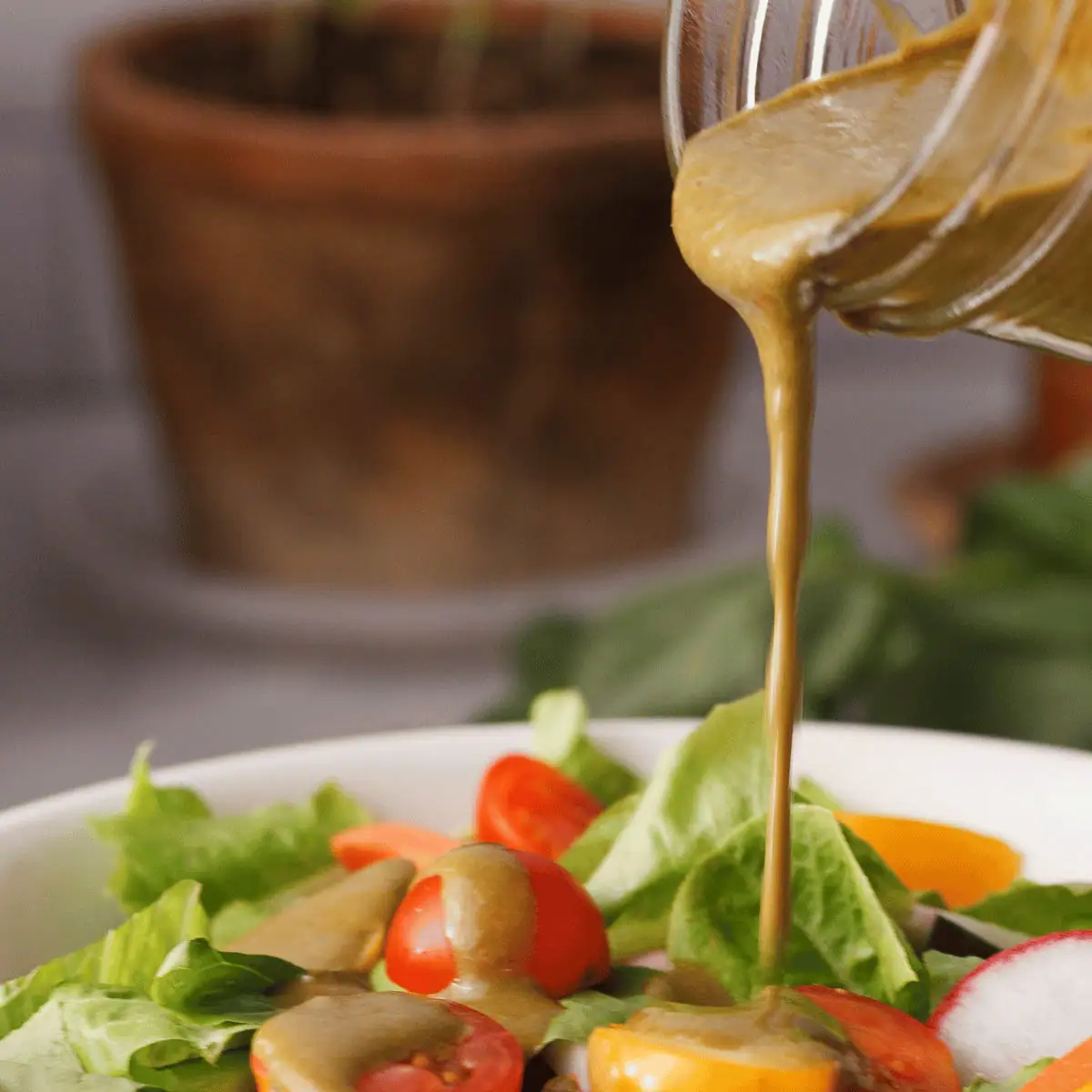 square image of balsamic basil vinaigrette pouring over salad
