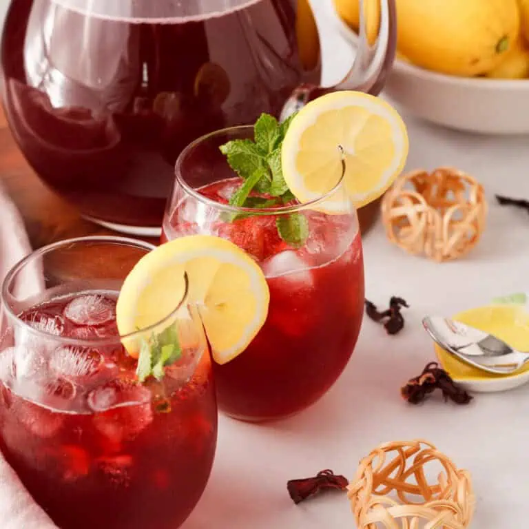 hibiscus lemonade in glasses topped with lemon slices and pitcher in the background
