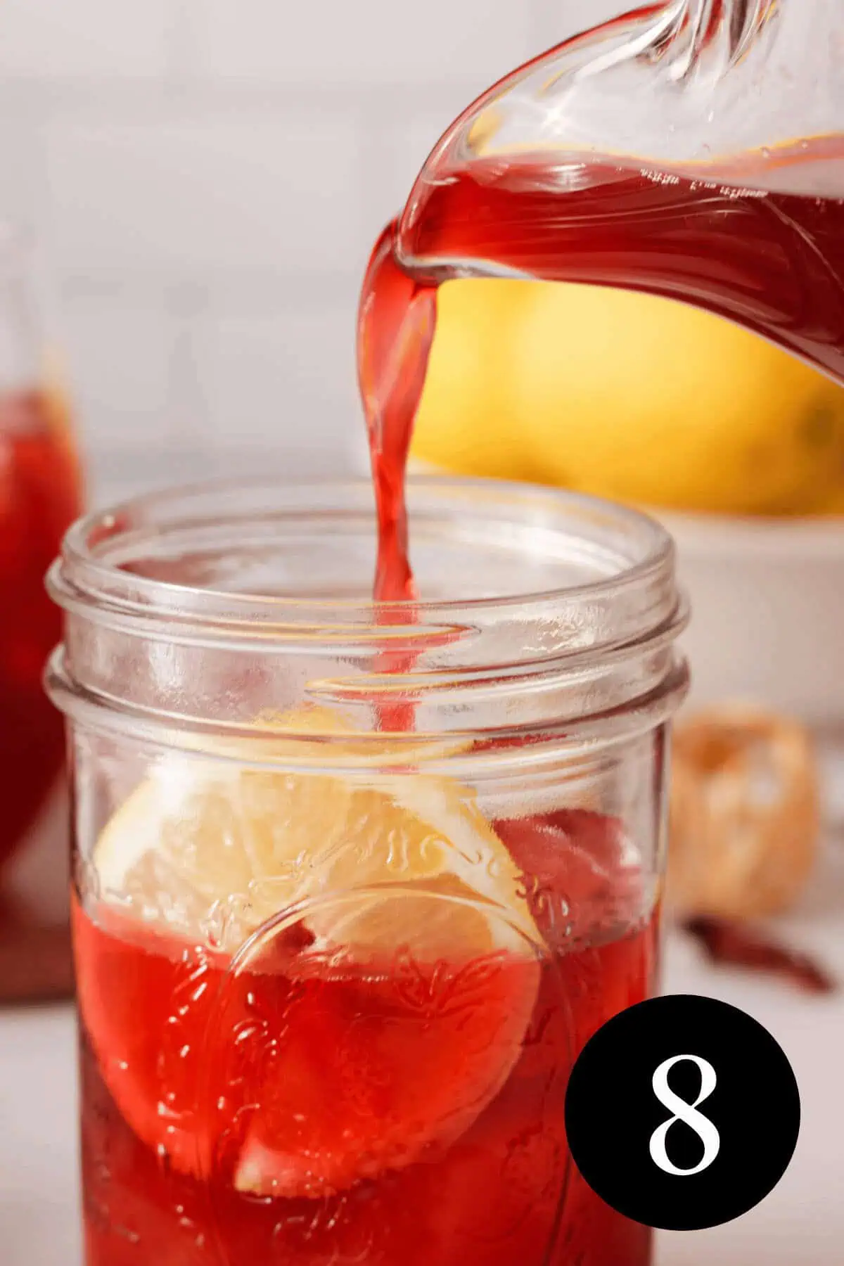 pouring hibiscus lemonade into mason jar filled with ice