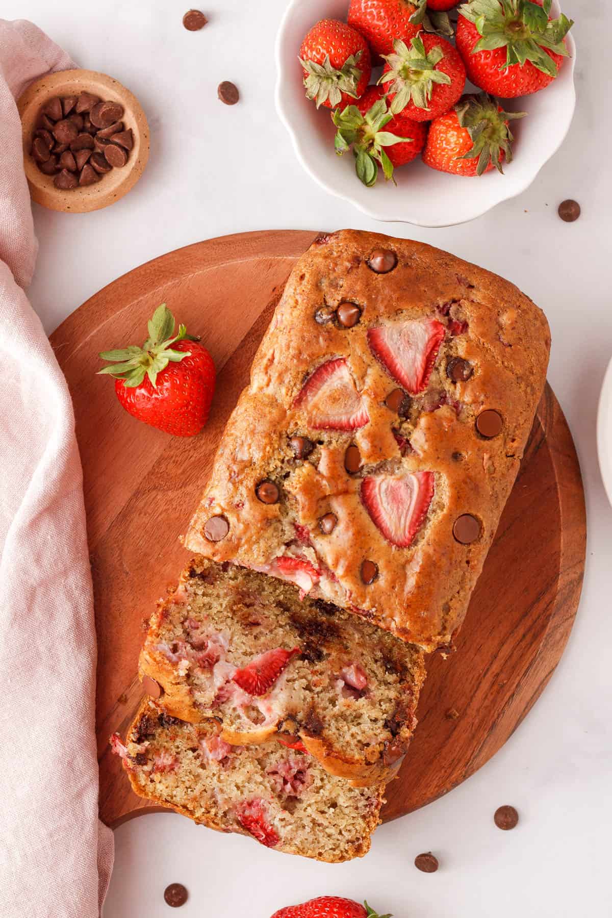 overhead image of strawberry chocolate chip bread on counter with extra strawberries and chocolate chips surrounding the loaf