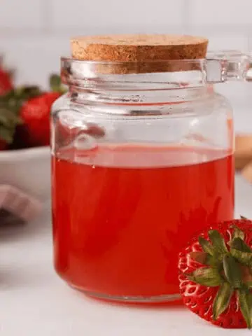 side image of strawberry top simple syrup in glass jar with extra strawberry tops propped on the jar