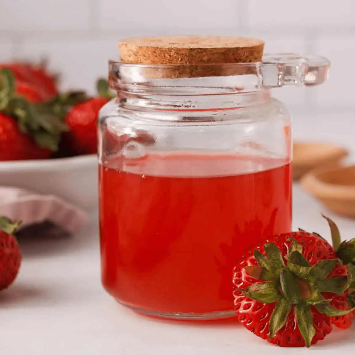 side image of strawberry top simple syrup in glass jar with extra strawberry tops propped on the jar