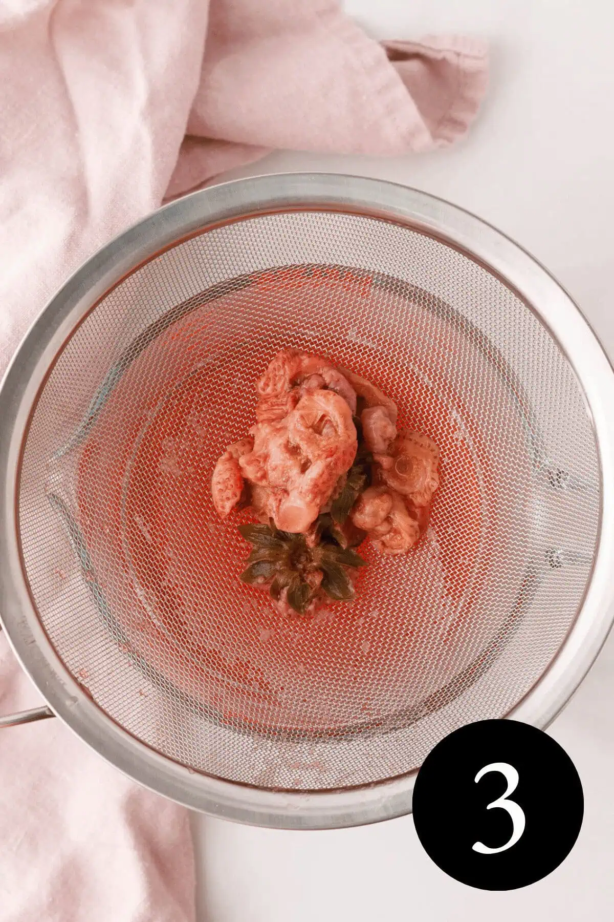 overhead image of strawberry tops sitting in mesh strainer over a liquid measuring cup