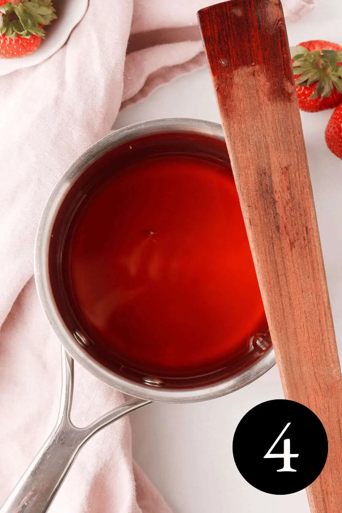 overhead image of strawberry top syrup in saucepan with stir stick resting on edge