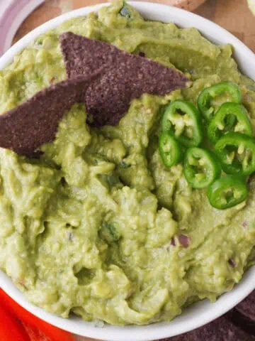 overhead closeup of guacamole in bowl with chips and sliced jalapenos accenting the top